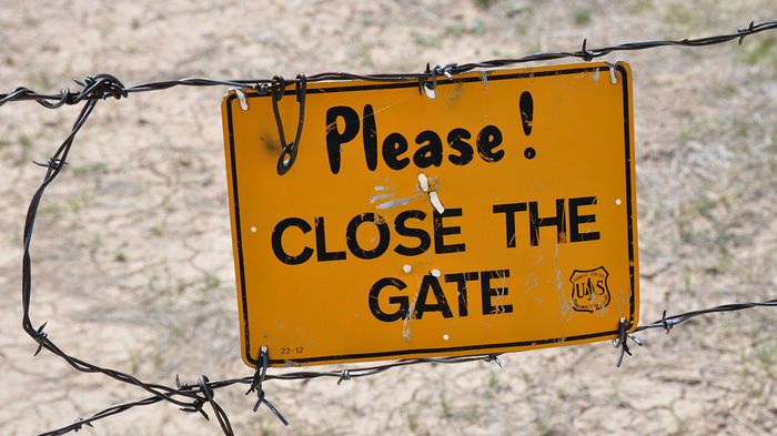 Fenced area with barbed wire and a sign reminding to close the gate.