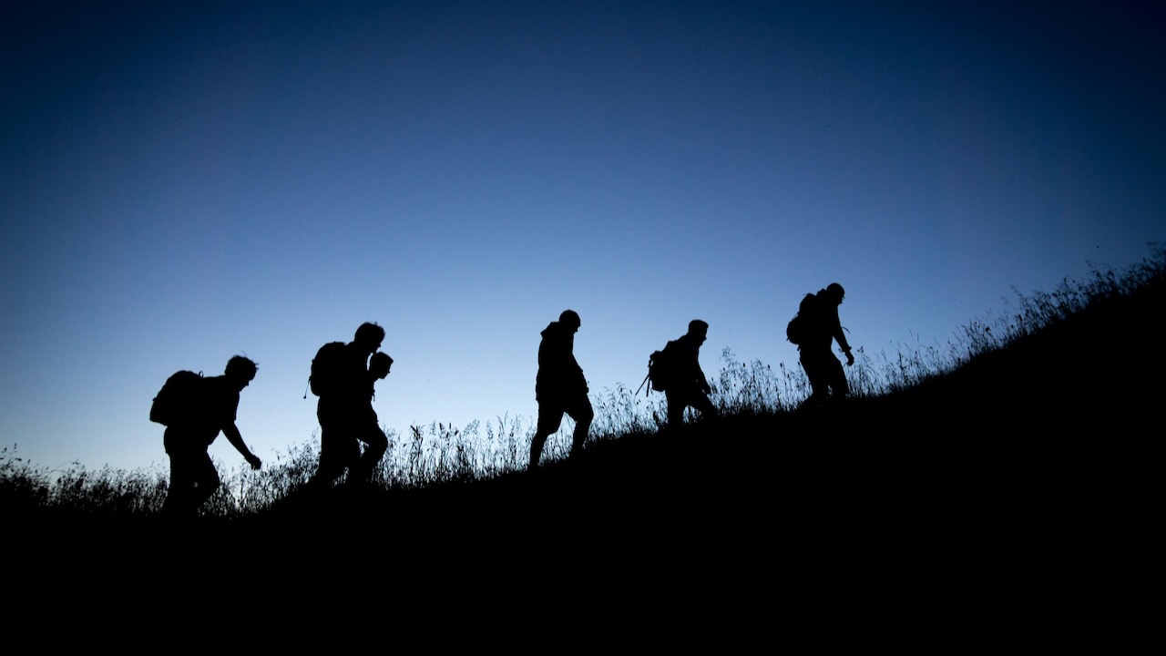 Silhouettes of 5 people hiking up a hill with a darkening blue sky background